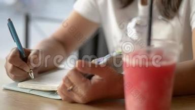 亚洲女人坐着写日记，用一杯冰沙果汁激励饮料店的生活。